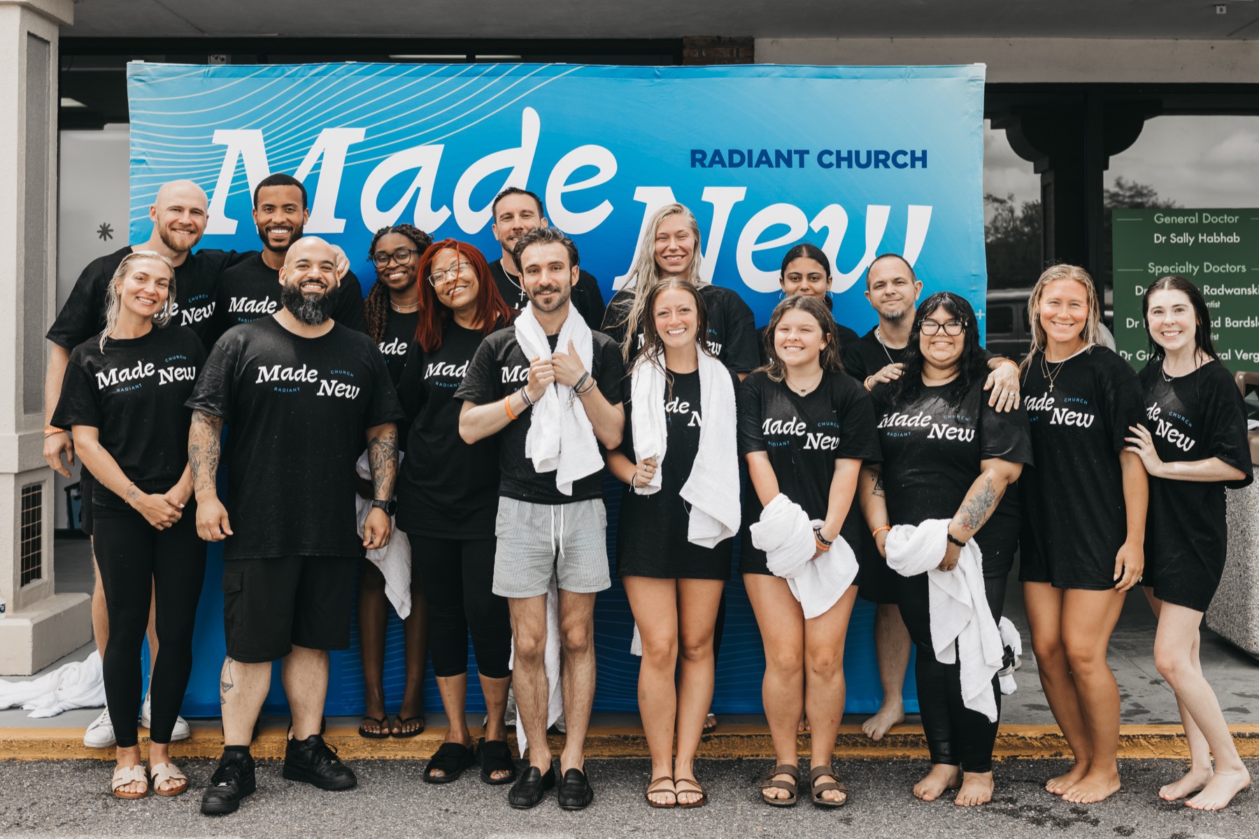 A baptism group stands in front of a Made New banner.